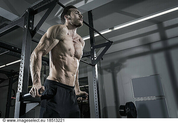 Shirtless muscular man doing dips exercise at the gym