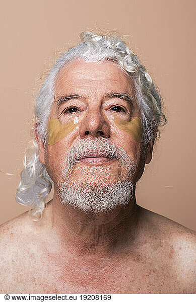 Shirtless senior man with gray hair and eye patch against beige background