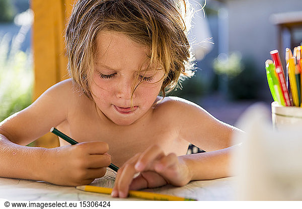 Shirtless 5 year old boy drawing with colored pencils