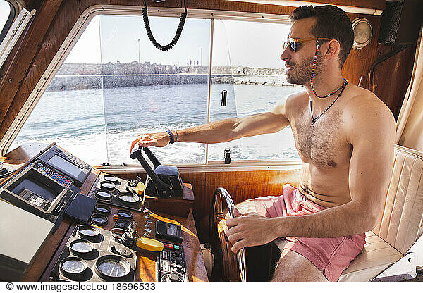 Shirtless young man driving yacht at vacation