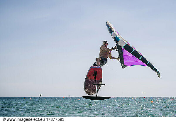 Shirtless young man with hydrofoil over sea on sunny day