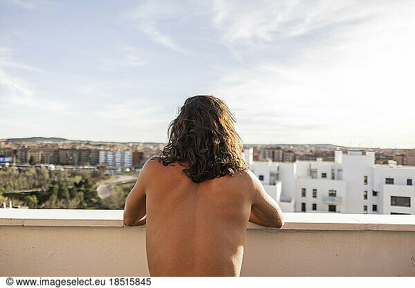 Shirtless young man with long hair standing on balcony