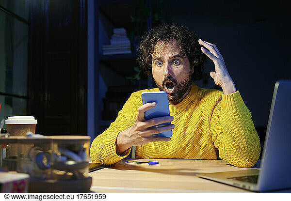 Shocked businessman holding mobile phone sitting at desk in office