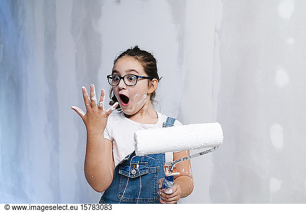 Shocked girl looking at her stained hand while painting a wall in a house