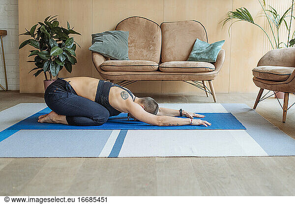 short haired woman doing yoga child pose in home with mat