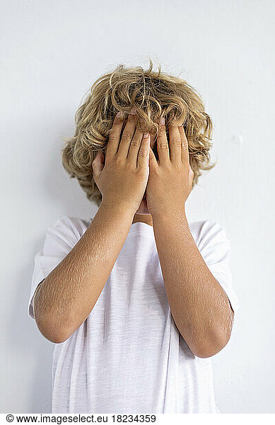 Shy boy covering face with hands against white background