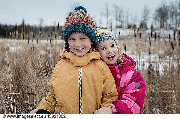siblings cuddling and laughing whilst playing outside in winter