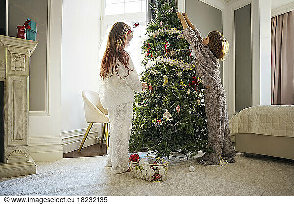 Siblings decorating Christmas tree in bedroom at home
