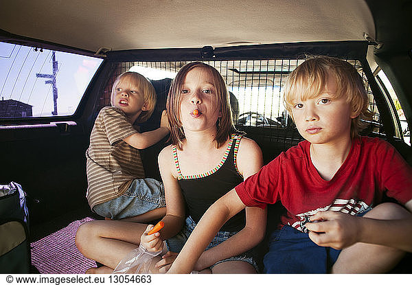 Siblings eating while sitting in car trunk
