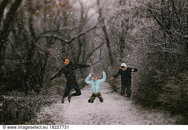 Siblings jump in snow storm in forest in winter