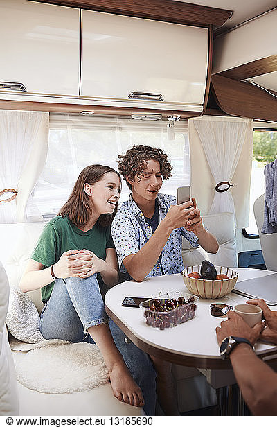Siblings looking at smart phone while sitting with father in camper van