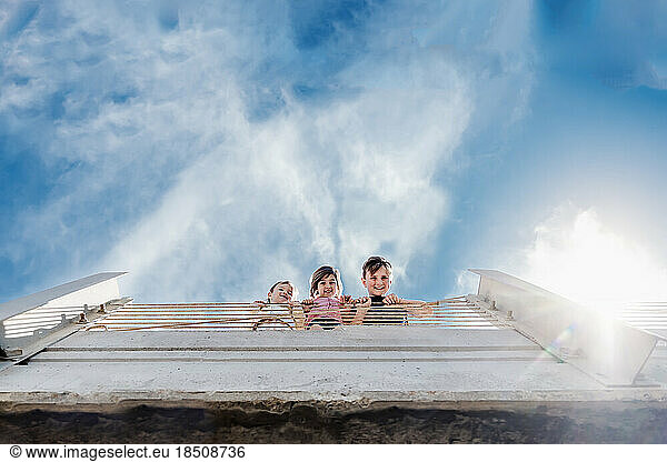 Siblings Looking Down Over Bridge Railing