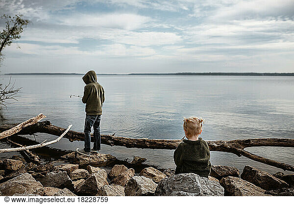 Siblings on lakeshore fishing on overcast early spring day