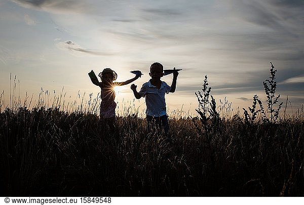 siblings playing outside in a meadow at sunset in summer