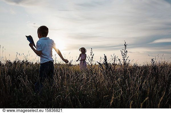siblings playing together outside at sunset with paper aeroplanes