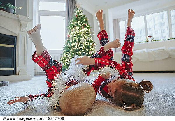 Siblings playing with tinsel sting on carpet at home