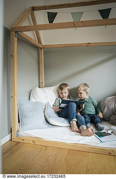 Siblings reading book while sitting in bedroom