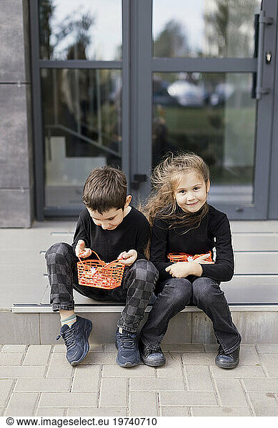 Siblings sitting on sidewalk and holding baskets for Halloween sweets