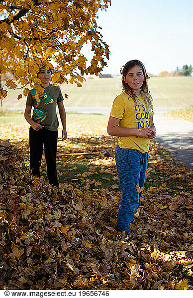 Siblings standing outside among maple tree and fallen autumn leaves