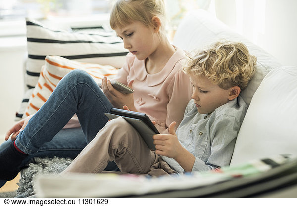 Siblings using technologies on sofa at home