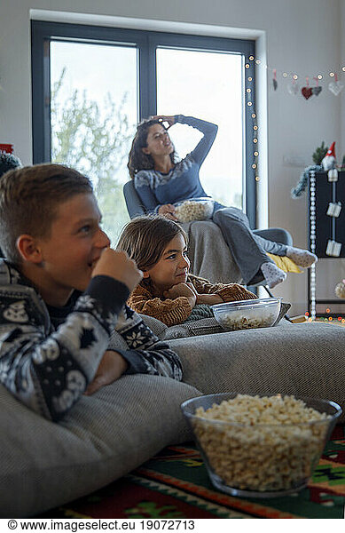 Siblings watching TV with mother and eating popcorn at home