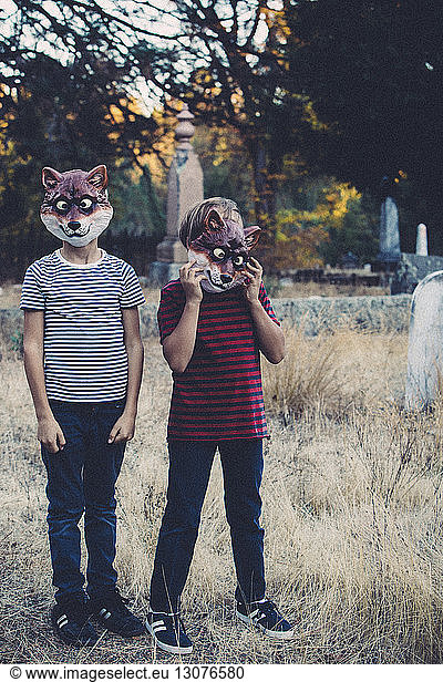 Siblings wearing animal masks while standing at cemetery