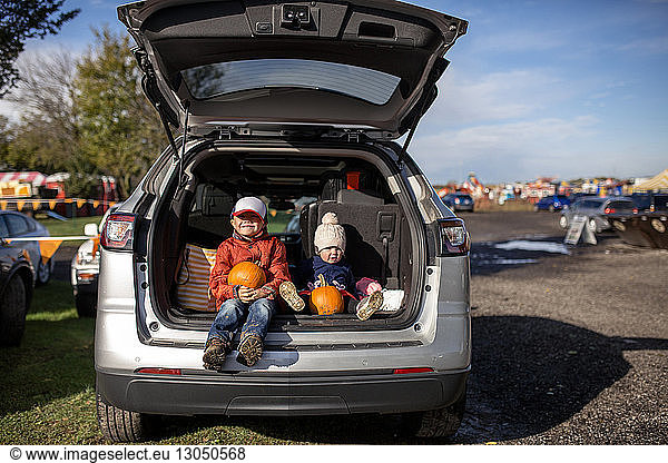 Siblings with pumpkins sitting in car trunk