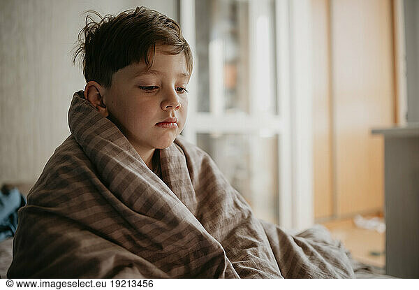 Sick boy wrapped in blanket at home