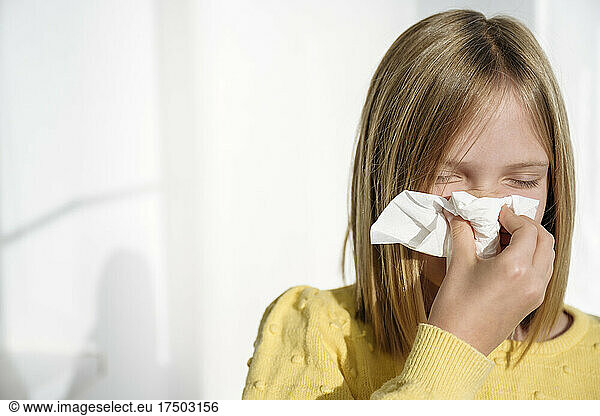 Sick girl blowing nose with tissue at home