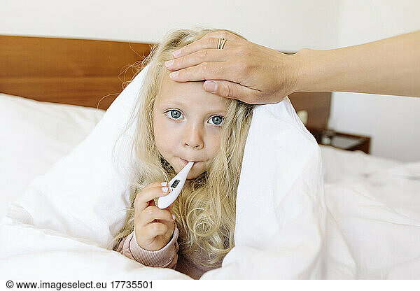 Sick girl measuring body temperature wrapped in blanket