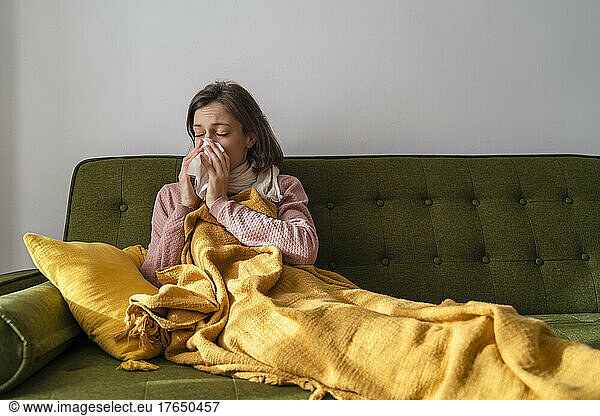 Sick woman blowing nose in facial tissue at home