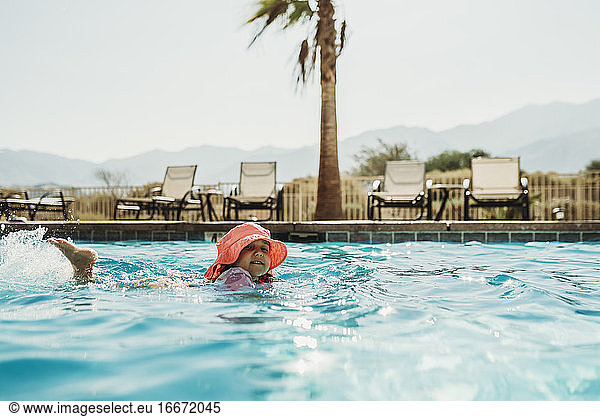 Side angle view of little girl in pink hat swimming in pool