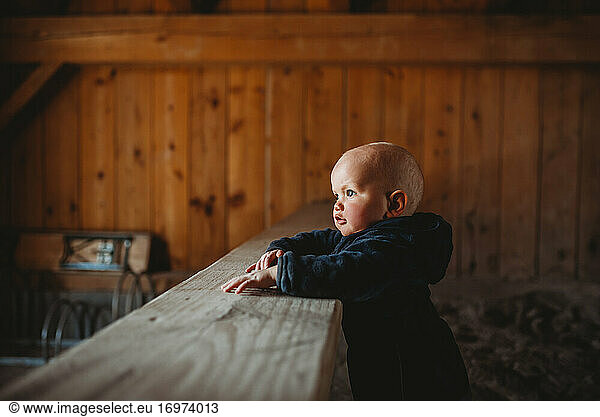 Side profile portrait of adorable baby boy with wooden walls farmhouse