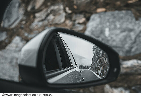 Side-view mirror reflection of car driving along alpine highway