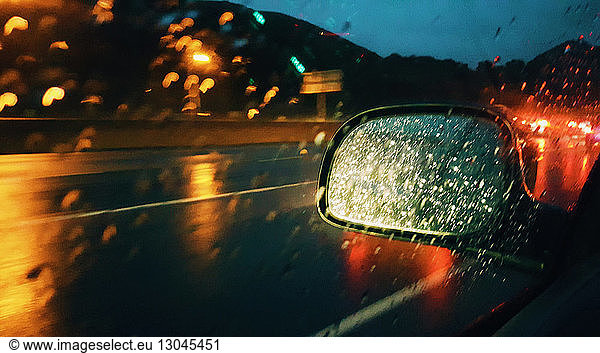 Side-view mirror seen through car window during rainy season at night