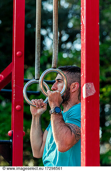Side view of a dark-haired athlete with beard training on gymnastic rings.