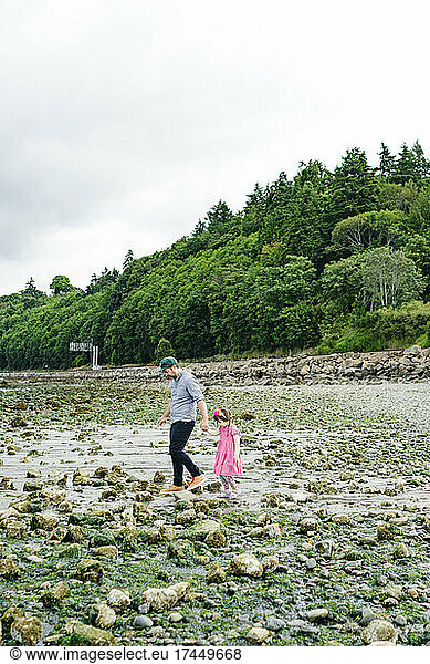 Side view of a father and daughter walking across a rocky beach