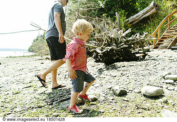 Side view of a father and son walking on a rocky beach on a sunny day
