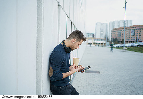 Side view of a modern man in casual clothes sitting near a white wall