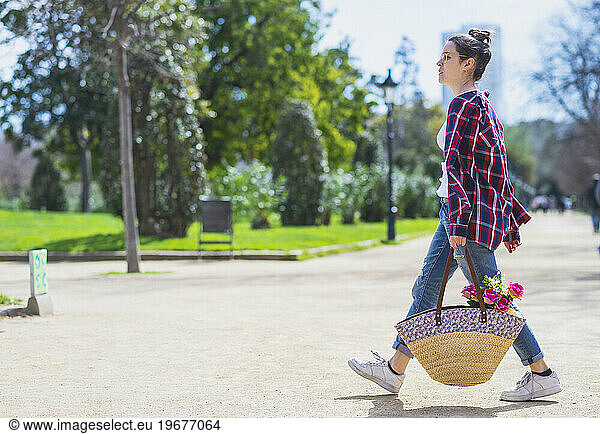 Side view of a young hipster woman holding a wicker basket while