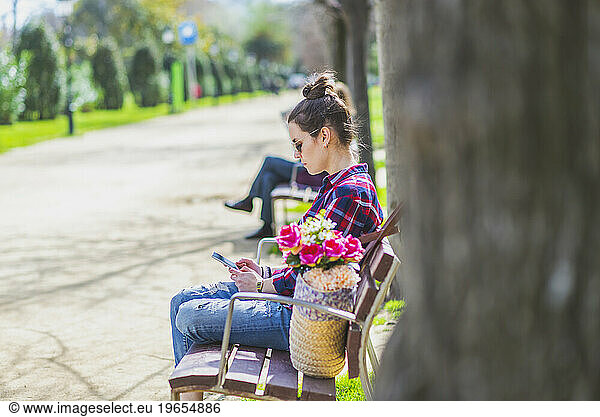 Side view of a young hipster woman sitting on a park bench relax