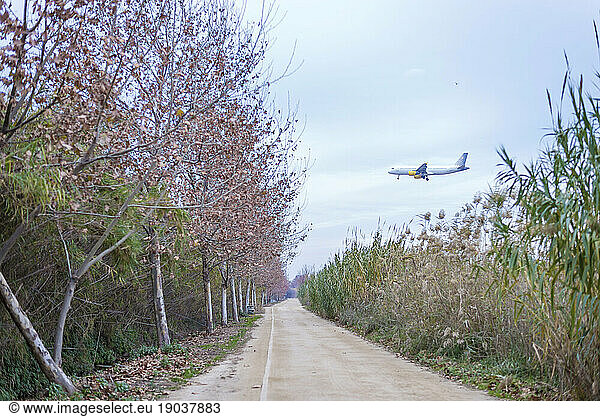 Side view of airplane taking off above a dirt road on a rural area near to airport