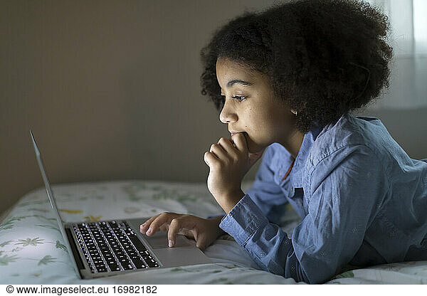 Side view of an ten year-old bi-racial girl working on her laptop