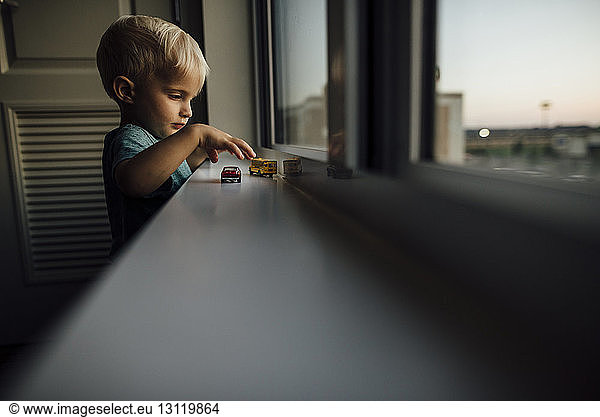 Side view of baby boy playing with toy cars on window sill at home