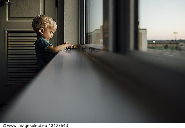 Side view of baby boy playing with toy cars on window sill at home during sunset