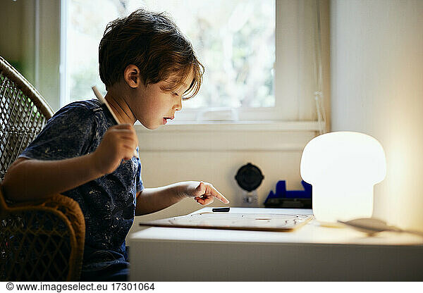 Side view of boy drawing while sitting on chair at home