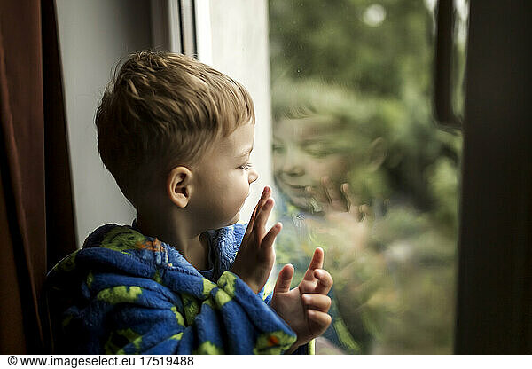 Side view of boy looking at his reflection in window