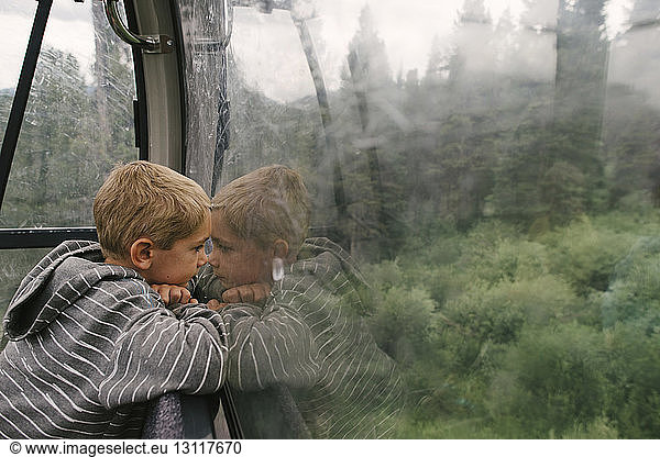 Side view of boy looking through window while traveling in overhead cable car