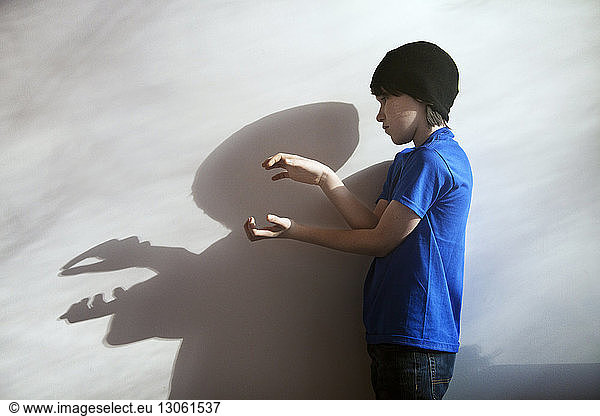 Side view of boy playing with shadow by wall at home