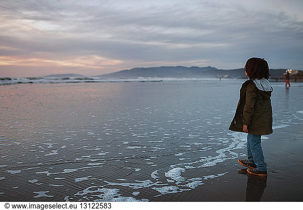 Side view of boy standing at Ocean Beach against cloudy sky